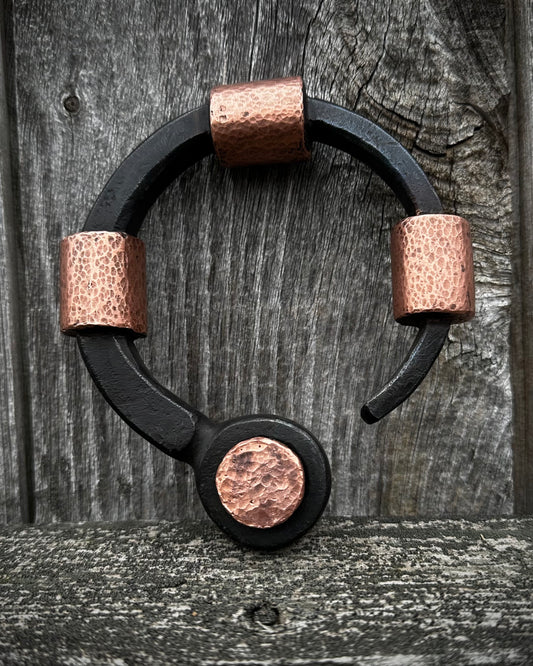 A black forged steel ring with hammered copper interiors, placed on a wooden surface.