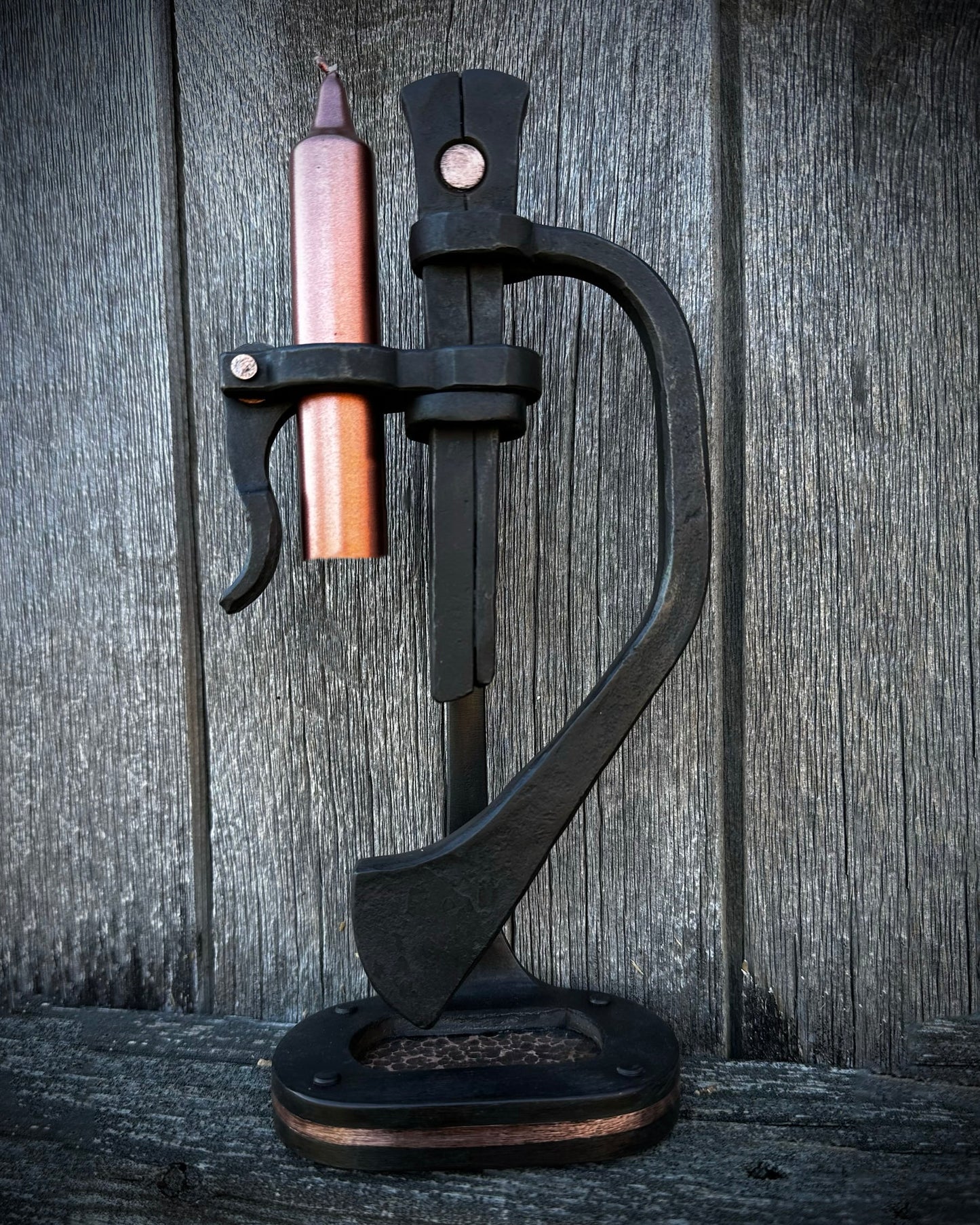 A black forged steel chamberstick with copper accents, designed to hold a candle, placed on a wooden surface.