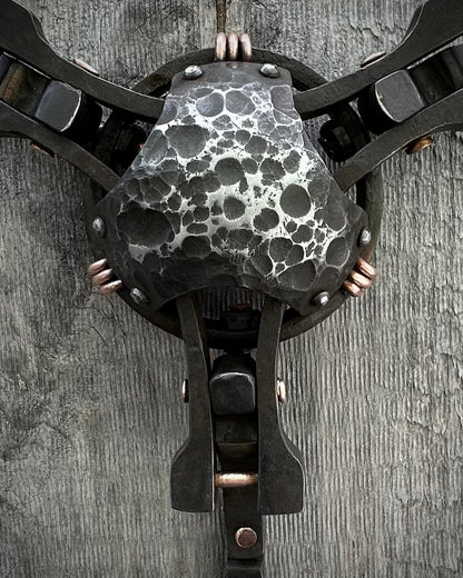 A close-up of a textured sculpture made of steel and copper with a patina finish, featuring a mix of smooth and rough surfaces, mounted on a wall.