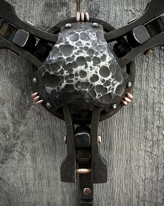 A close-up of a textured sculpture made of steel and copper with a patina finish, featuring a mix of smooth and rough surfaces, mounted on a wall.